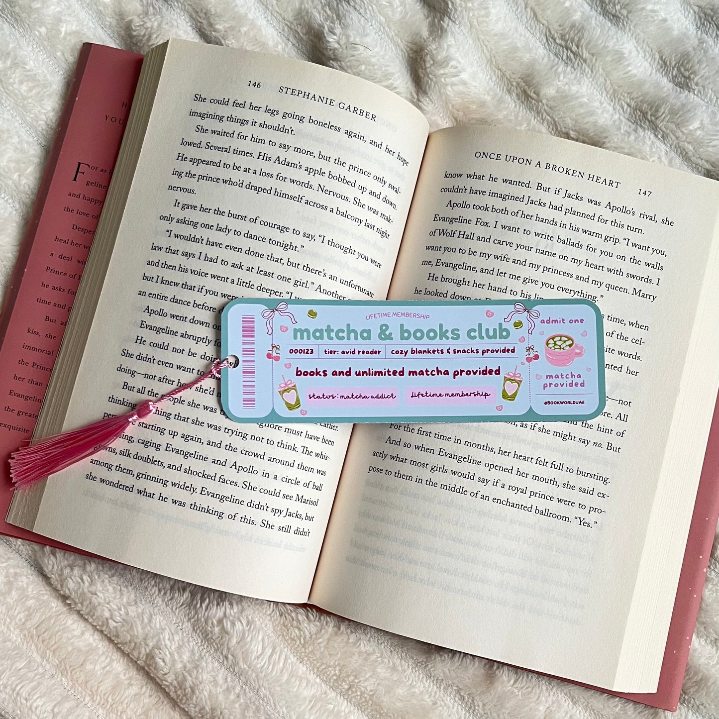 Open book with a bookmark featuring 'matcha & books club' on a fluffy white surface