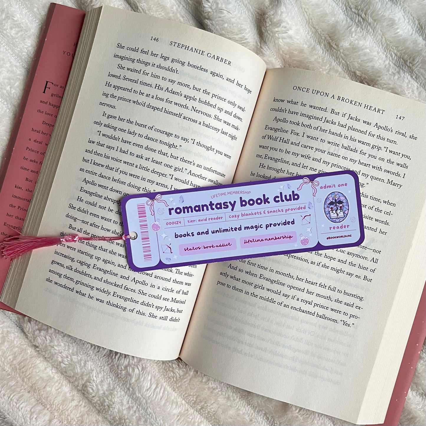 Open book with a 'Romantasy Book Club' bookmark on a fluffy surface