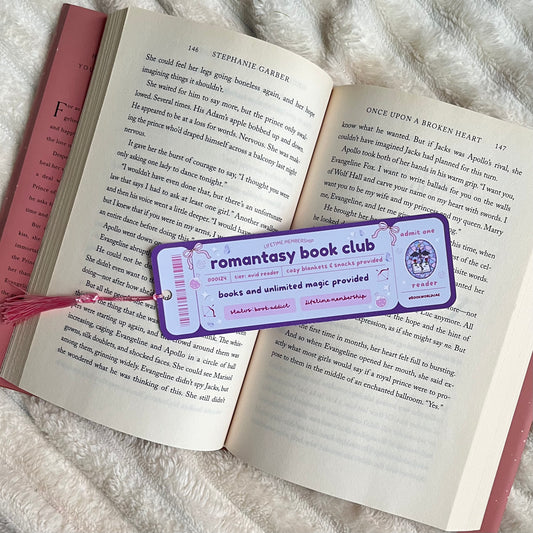 Open book with a 'Romantasy Book Club' bookmark on a fluffy surface