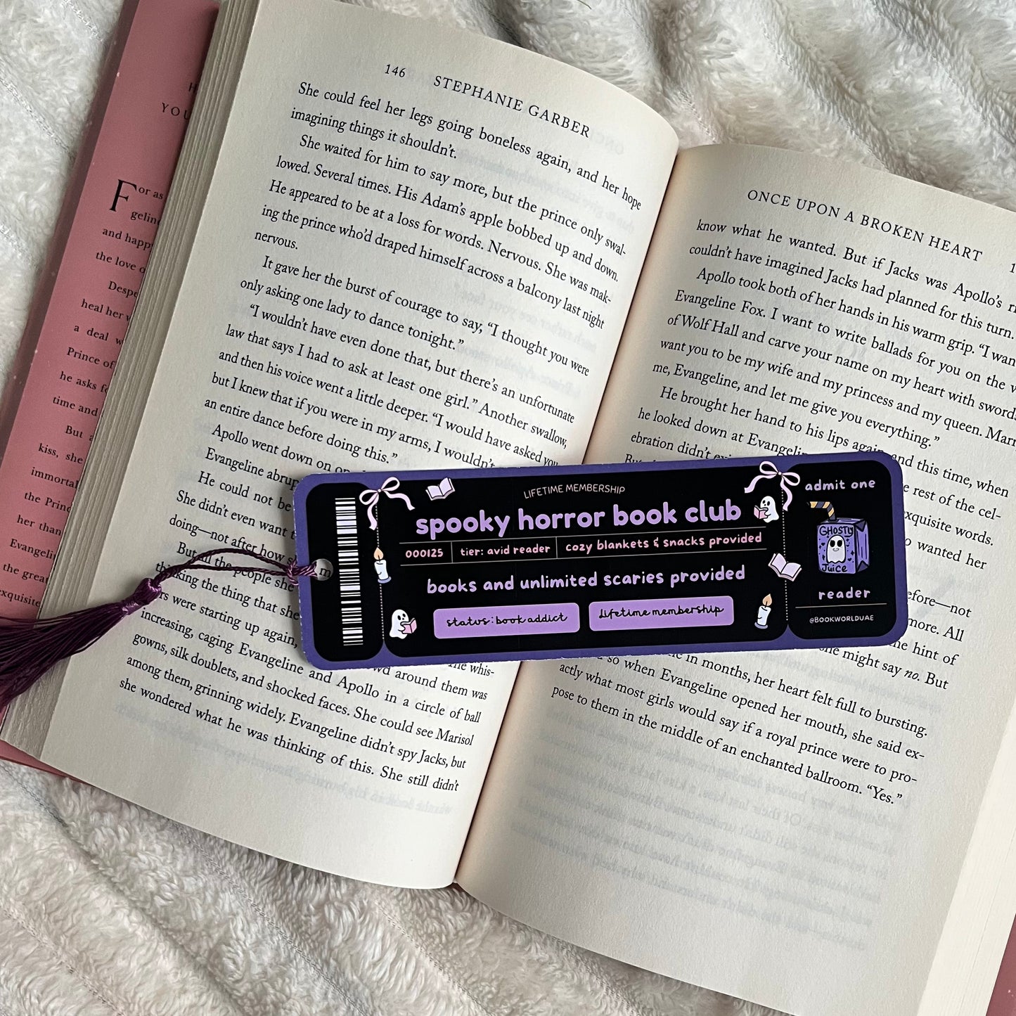Open book with a Spooky Horror Book Club bookmark on a fluffy white surface